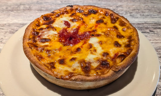 A Felix & Oscar's Cheese Topper pizza. The crust is topped with cheese, then toppings and sauce, then another layer of cheese on top.